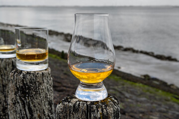 Tasting of dram single malt scotch whisky on seashore in Scotland, old wooden pole with whisky glass