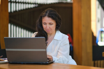 smiling mature businesswoman drinking coffee while working in cafe