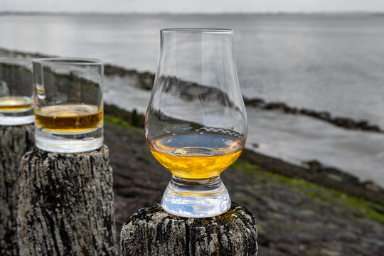 Tasting of dram single malt scotch whisky on seashore in Scotland, old wooden pole with whisky glass