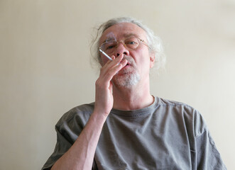 A middle-aged man, wearing glasses, takes a drag on his cigarette and looks directly into the camera.