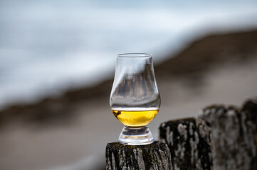 Tasting of dram single malt scotch whisky on seashore in Scotland, old wooden pole with whisky glass