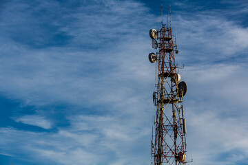 Telecommunication pole with several kinds of antennas in blue sky and clouds in sunny bright day with copy space