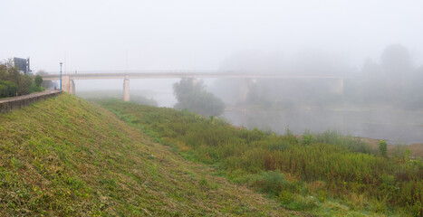 Landscape with Sava river, promenade on riverbank embankment and concrete bridge over the river during misty autumn morning