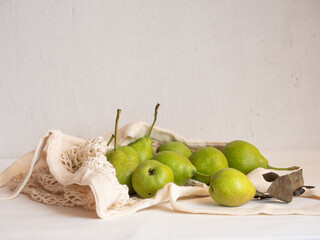 Ripe garden green pears in a light cotton string bag on a white background in the morning light