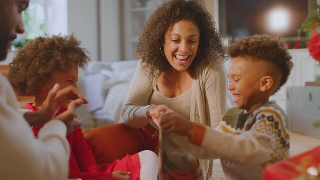 Boy unwrapping present as family exchange gifts around christmas tree at home - shot in slow motion