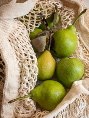 Ripe garden green pears in a light cotton string bag on a white background in the morning light