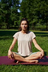 Naklejka na ściany i meble yoga class, pacification, meditation, outdoor sports, self-awareness. young beautiful woman sits in Padmasana lotus position on a green lawn among green trees