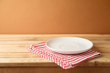 Empty white plate on wooden table with tablecloth.  Kitchen mock up for design and product display.