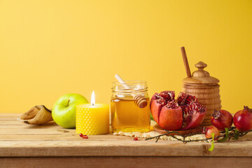Jewish holiday Rosh Hashana concept with honey jar, apple and pomegranate on wooden table over yellow background
