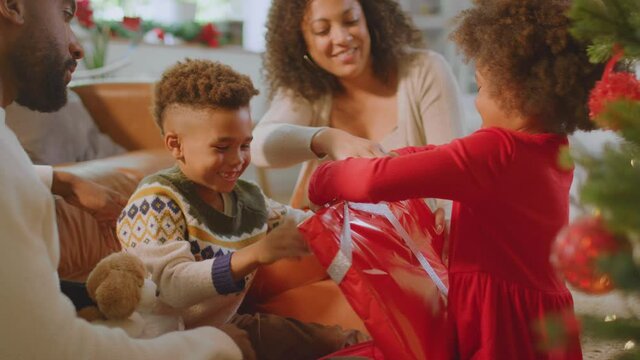 Girl unwrapping present as family exchange gifts around christmas tree at home - shot in slow motion