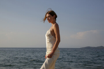 Outdoor portrait of woman in white long silk camisole dress. Summer wedding season fashion.