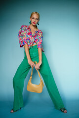Summer fashion: confident blonde woman wearing colorful blouse, green high waist wide leg jeans,...