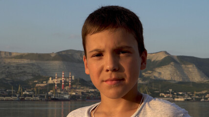 Fototapeta na wymiar Portrait of a boy. Sunlight at sunset. Swarthy, serious face. Dark hair. Against the background of an industrial facility and mountains. Close-up.