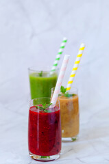 Top view of three different fresh delicious smoothies in a glasses made of peach, banana and berries with mint. Creative concept of healthy detox drink, diet or vegetarian food concept. Copy space.