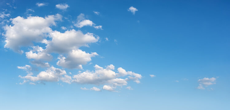Beautiful spring sky with few white fluffy clouds on a sunny day. Clear bright blue summer sky for weather forecast, vacations and travel season ideas. Sky only panoramic image. Wide azure skyscape.