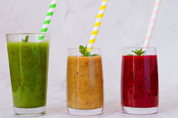Top view of three different fresh delicious smoothies in a glasses made of peach, banana and berries with mint. Creative concept of healthy detox drink, diet or vegetarian food concept. Copy space.