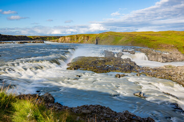 Long exposure motion blurred flow of huge river in Southern Iceland. Green hills, sunny summer day.