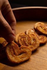 a hand taking delicious freshly baked puff pastry ears on a wood colored board