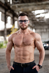 Muscle sexy naked young man without shirt poses in abandoned warehouse with black car in the...