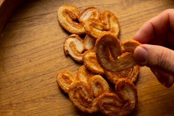 a hand taking delicious freshly baked puff pastry ears on a wood colored board