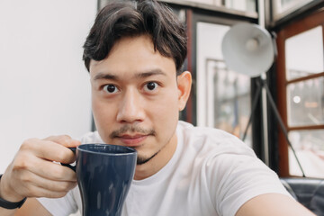 Happy Asian man is drinking hot drink coffee in the cafe.