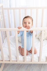 a cute baby boy is standing in a crib in the nursery and holding on to the side with his hands