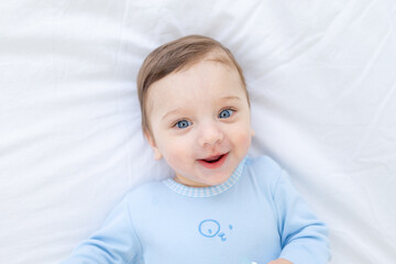 smiling baby boy on the bed in a blue bodysuit, portrait of a happy healthy little baby