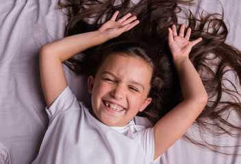 a happy little brunette girl in pajamas is lying on the bed linen on the bed with her eyes closed