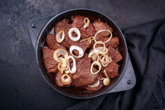 Traditional Filipino dry aged angus bistek tagalog steak with onion rings in soy sauce served as top view in a cast-iron casserole