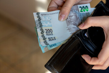 woman putting Brazilian money bills from her wallet.