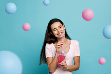 Young girl drinking fresh juice from plastic cup take-out food. Woman with berry lemonade on blue background. Summer cold drinks.