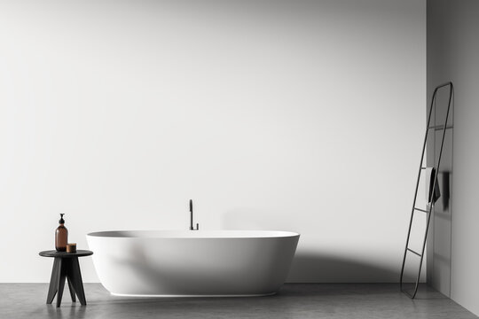 Grey minimalist bathroom area with oval ceramic bathtub and dark wood stool