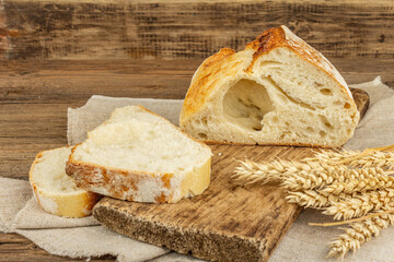 Freshly baked bread with wheat ears, fragrant pieces on a cutting board