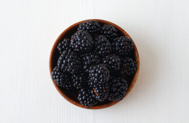 Ripe blackberries, wooden bowl with fresh blackberries from local farmers market on white wooden table. Flat lay, top down view.