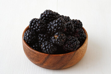 Ripe blackberries, wooden bowl with fresh blackberries from local farmers market, high angle view on white wooden table.