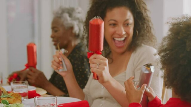 Multi generation family sitting around table at home pulling crackers before eating Christmas meal - shot in slow motion 