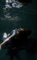 Fototapeta na wymiar A beautiful girl in a blue dress swims underwater in the pool like a little mermaid from a fairy tale