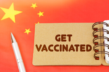 On the flag of China lies a notebook with the inscription - Get vaccinated