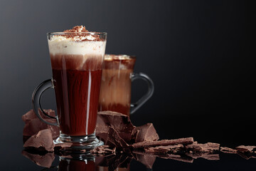 Hot chocolate with whipped cream and pieces of dark chocolate on a dark background.