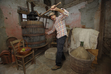 Mid-aged winemaker using an old wooden press in the space for winemaking