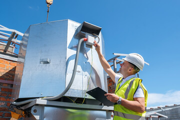Engineer with clipboard checking the installation of the ventilation system HVAC fan on the roof
