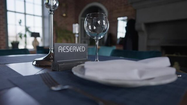 Male hand putting drinking glass on table with Reserved sign. Unrecognizable Caucasian waiter setting table in luxurious restaurant indoor in slow motion