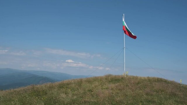 Bulgarian flag dancing on the wind on the top of Ruj summit and a clear blue sky behind
