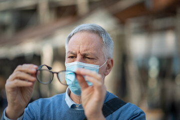 Man cleaning his eyeglasses fogged due to the mask, covid coronavirus vision concept