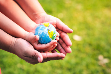 Eco Friendly Concept. The hands of children and adults are holding the world safe from global...