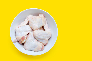Fresh raw chicken wings in white bowl on yellow background.