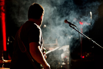 Guitar player staying in front of a microphone with a smokey, with shining background