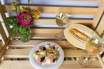 Salad with Green grape, ripe melon, meat, basil leaf and white wine, red and yellow flowers in vase on wooden box background