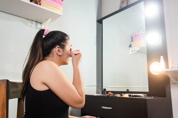 Beautiful concentrated girl applying makeup powder in front of the mirror in her room.