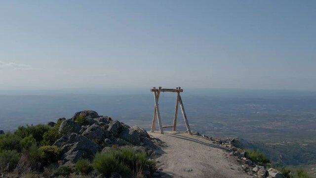 Drone pushes over a swing on a hilltop overlooking a valley.